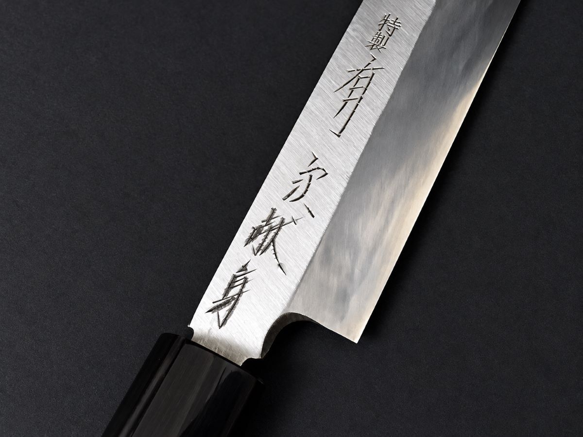 Close-up of Japanese kanji engraving on an Aritsugu knife blade with a black handle