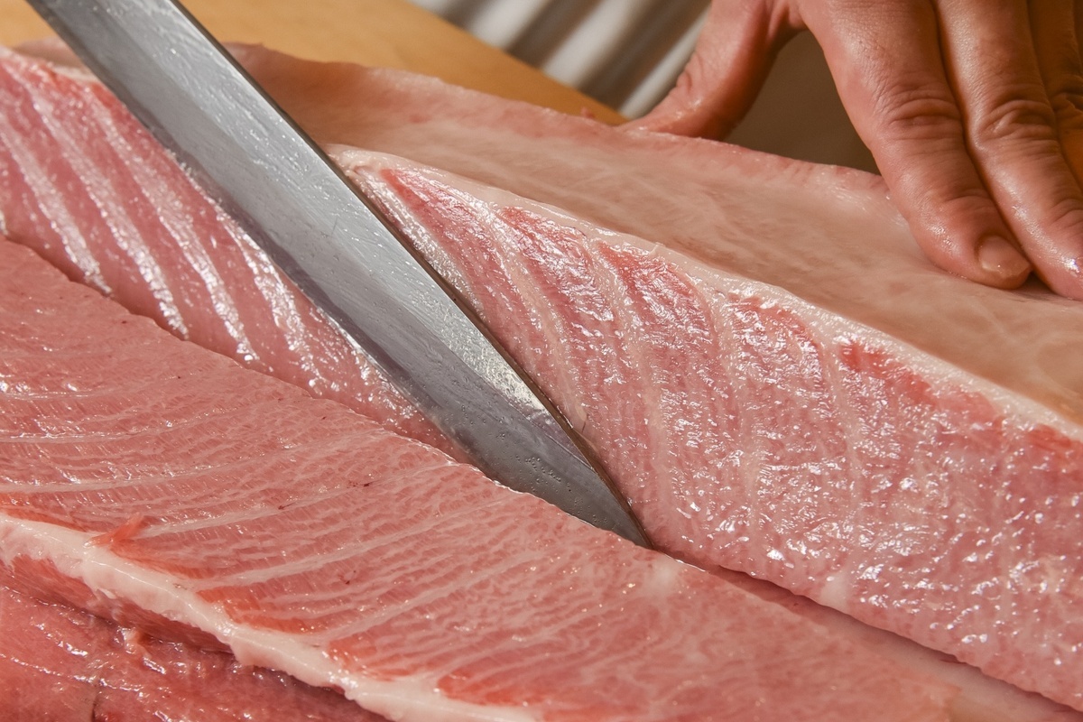 Close-up of a Japanese knife slicing a tuna fillet on a wooden cutting board for sashimi preparation